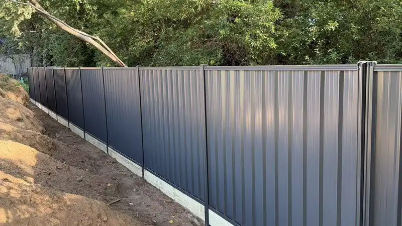 Monument colour colorbond-style steel fence installed in a Canberra residential boundary project with timber plinth and long fence line