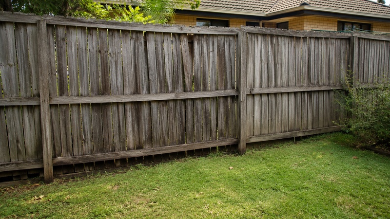 Aged timber fence panels showing fading cracking warping and maintenance issues in outdoor conditions